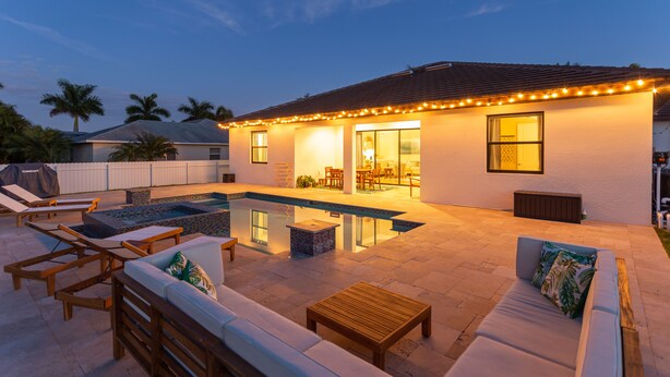 Un patio trasero con piscina, mobiliario exterior e iluminación colgante en la casa.