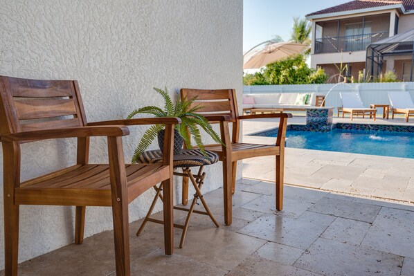 Zona de piscina con sillas de madera y una planta en maceta.