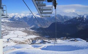 Un télésiège avec en toile de fond des montagnes majestueuses, un paysage enneigé et un ciel dégagé.