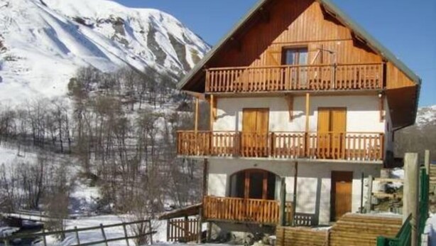 Eine zweistöckige Holzchalet mit Balkon, Pool und verschneitem Bergpanorama.