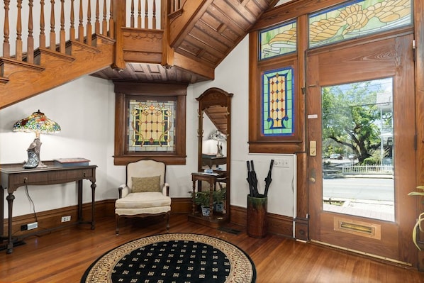 A wooden staircase, a stained glass window, a door with a view, a chair, a table, and a rug.