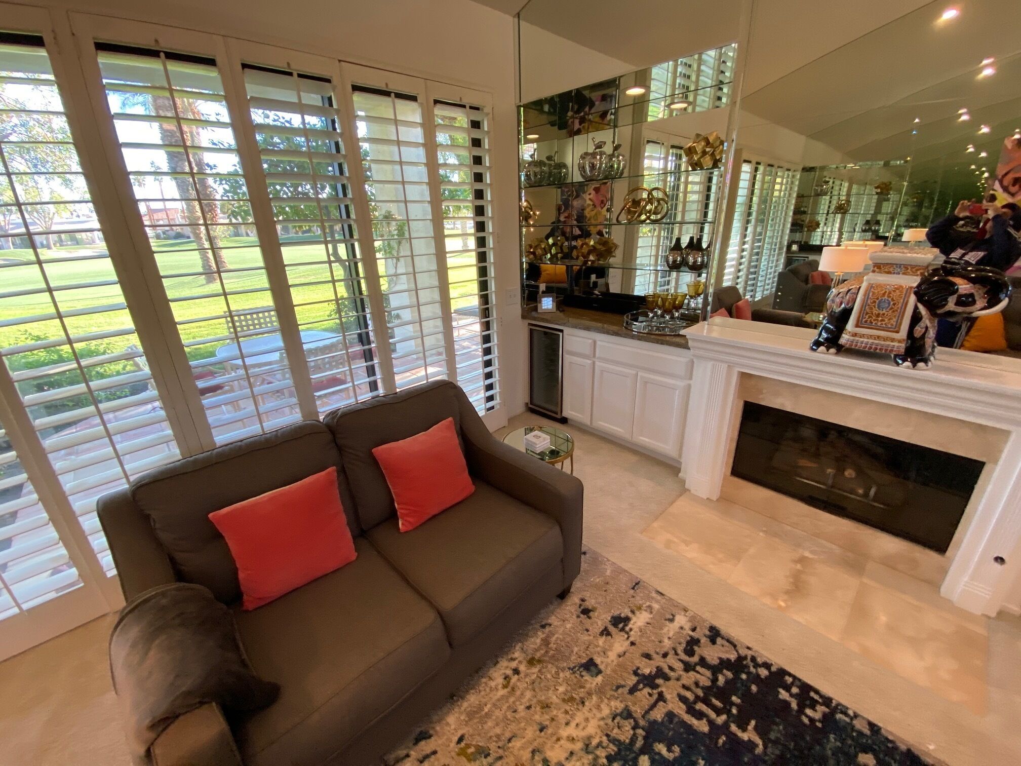 A living room with a brown sofa, red cushions, a fireplace, and a kitchen area with decorative items.