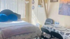 Een slaapkamer met een bed, een plafondventilator, een bureau met stoelen en een schilderij aan de muur.