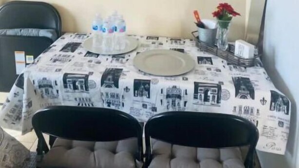 Een eetgedeelte met een tafel gedekt voor twee personen, een schilderij van een zonsondergang boven het water en een bord met de tekst 'COURAGE'.