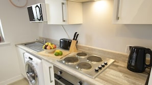 A compact kitchen with a washing machine, a stovetop with four burners, a toaster, and a coffee maker. - 1 bed Apartment Close to Football Grounds (Liverpool)
