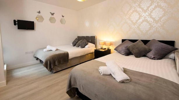 A hotel room with two beds, a flat-screen TV, decorative wall art, and a patterned wallpaper. - 1 bed Apartment Close to Football Grounds (Liverpool)