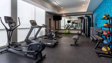 A gym with treadmills, elliptical machines, a bench, and a weight rack with medicine balls.