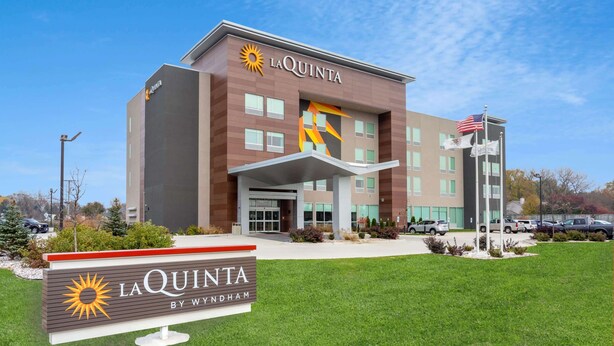 Un hôtel La Quinta au design moderne, avec un logo solaire bien visible et une enseigne indiquant qu’il fait partie du groupe Wyndham.