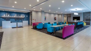 Un hall d’hôtel moderne, doté d’espaces aménagés avec des sièges, d’un comptoir d’accueil et d’une œuvre d’art murale représentant un paysage urbain.