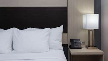 A hotel room with a bed, white pillows, a bedside table with a lamp, and a phone.