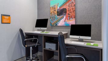 Ein moderner Arbeitsbereich mit zwei Schreibtischen, jeweils ausgestattet mit einem Computermonitor, einer Tastatur und einer Maus. Auf dem linken Schreibtisch steht ein Drucker, darüber an der Wand hängt ein großes, farbenfrohes Kunstwerk.