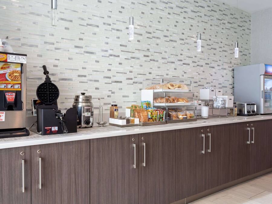 A breakfast bar with a waffle maker, coffee machine, and a refrigerator.