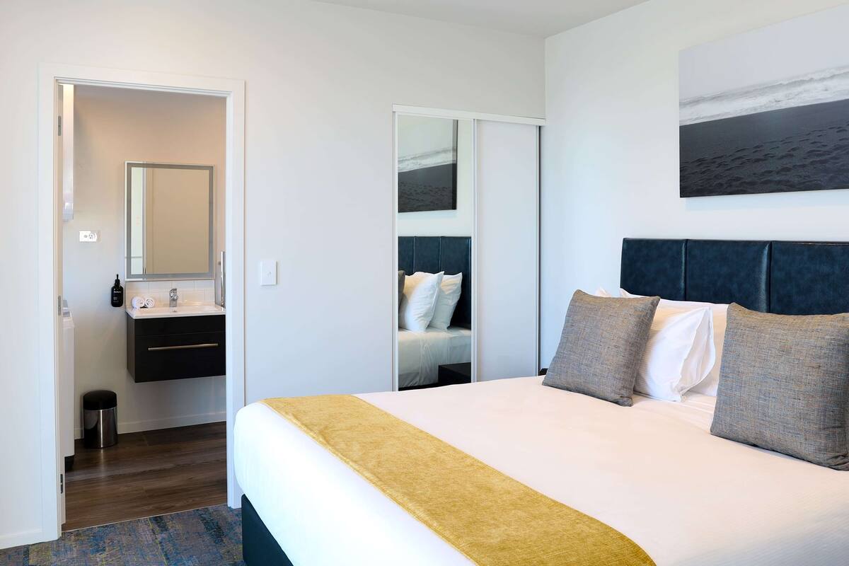 Ein Hotelzimmer mit Bett, Nachttisch, Spiegel, Kleiderschrank und einem Bild an der Wand.