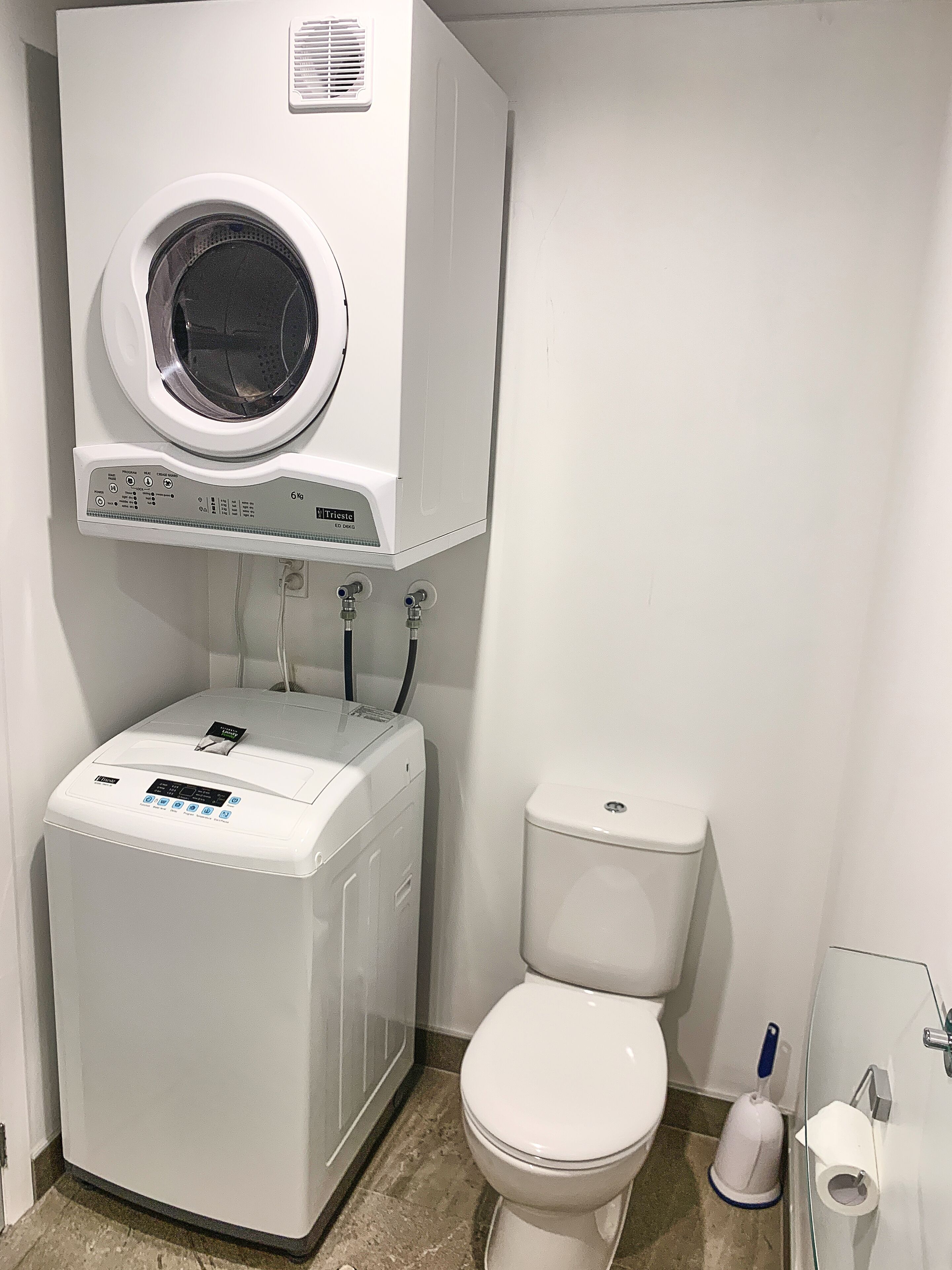 A compact bathroom with a washing machine, toilet, and a small trash bin.