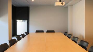 Un salón de conferencias con una larga mesa y sillas, un proyector y una ventana con persianas.