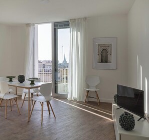 Ein modernes Wohnzimmer mit Essbereich, einem großen Fenster mit Vorhängen, einem Flachbildfernseher und einem gerahmten Bild an der Wand.