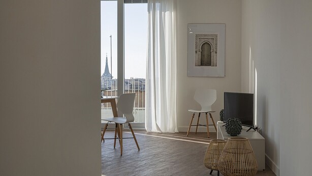 A modern living room with a large window, a framed artwork, a flat-screen TV, and a dining area with chairs.