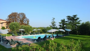 A pool area with lounge chairs and umbrellas, surrounded by greenery and trees. - Agriturismo Colombare Teboi (Colombare)