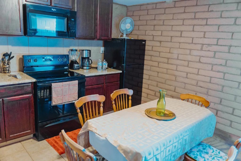 Une cuisine compacte équipée d’un four à micro-ondes, d’une cuisinière et d’un réfrigérateur. On y trouve une table à manger avec des chaises et un ventilateur fixé au mur.
