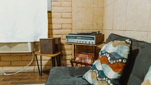 Tunnelmallinen olohuone, jossa on harmaa sohva, kuviollinen koristetyyny, vanhanaikainen radio ja pieni pöytä, jonka päällä on kaiutin.