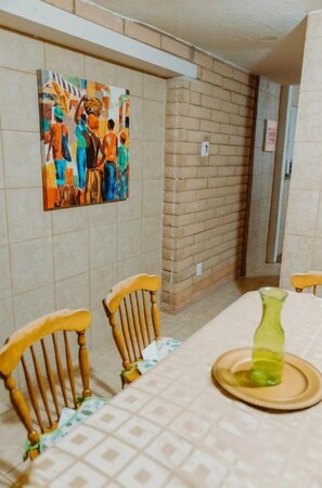 A dining area with a table set for two, a green vase, and a colorful abstract painting on the wall.