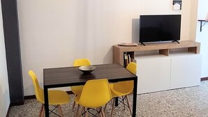 Una sala moderna con una mesa de comedor de madera oscura, sillas amarillas, un televisor de pantalla plana sobre un mueble de madera y un cuadro minimalista en la pared.