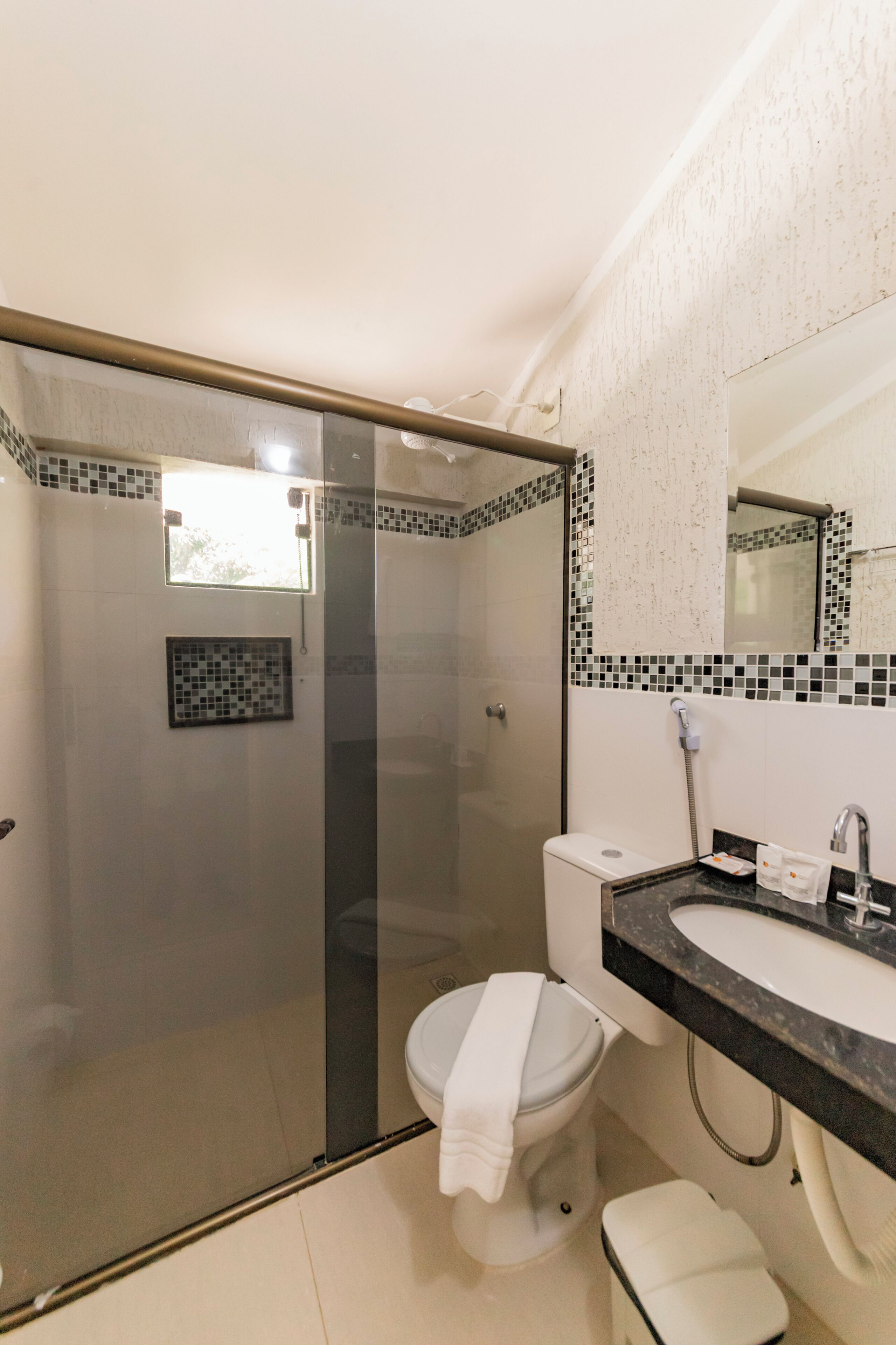 A bathroom with a glass-enclosed shower, a white toilet, a sink with a black countertop, and a tiled backsplash.