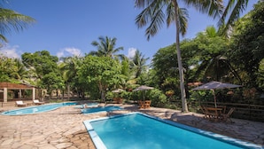 A pool area with stone flooring, lounge chairs, and umbrellas. - Pousada Ponta de Mangue (Maragogi)