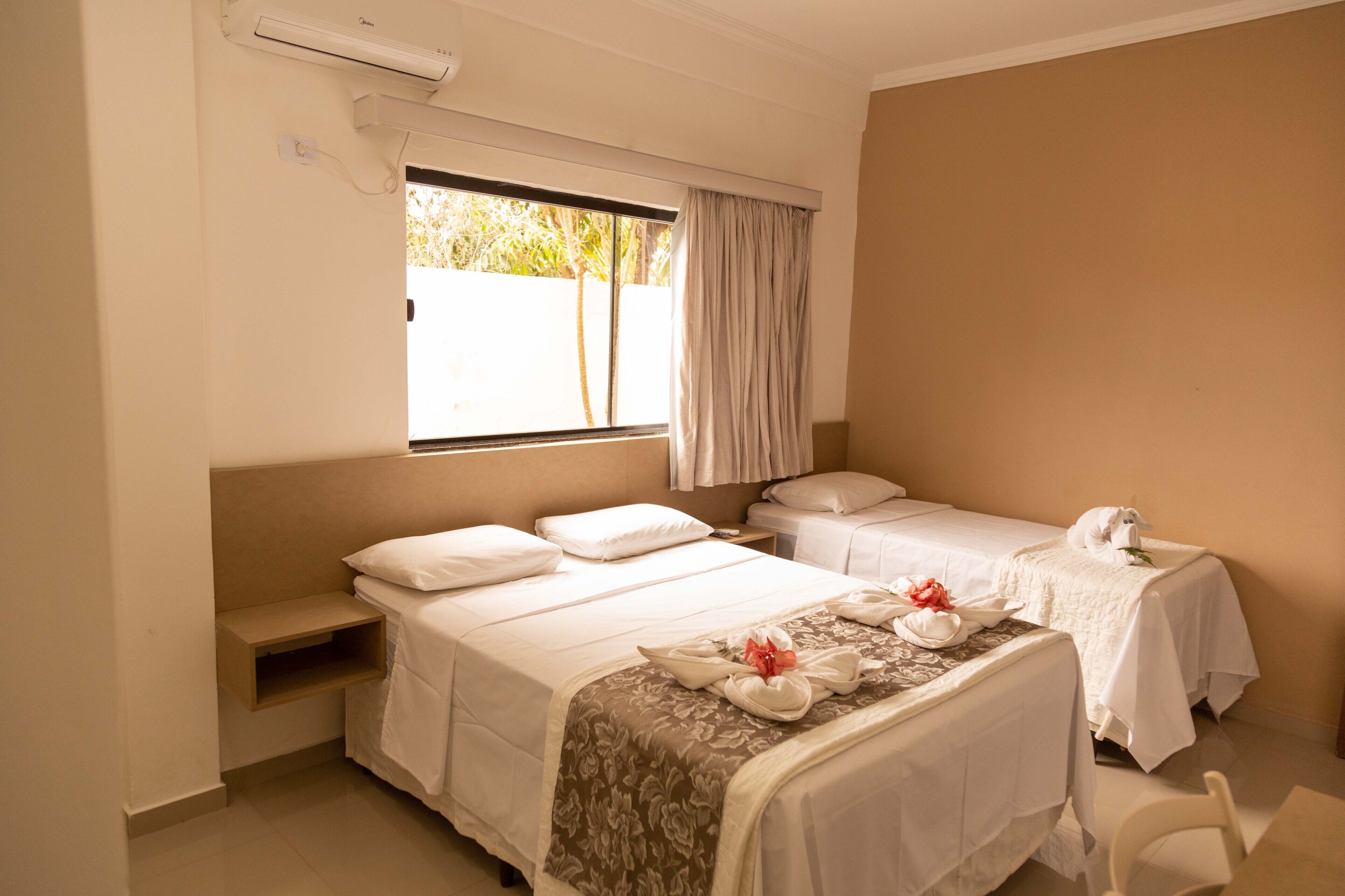 A hotel room with two beds, a window with curtains, a bedside table with a phone, and a chair.