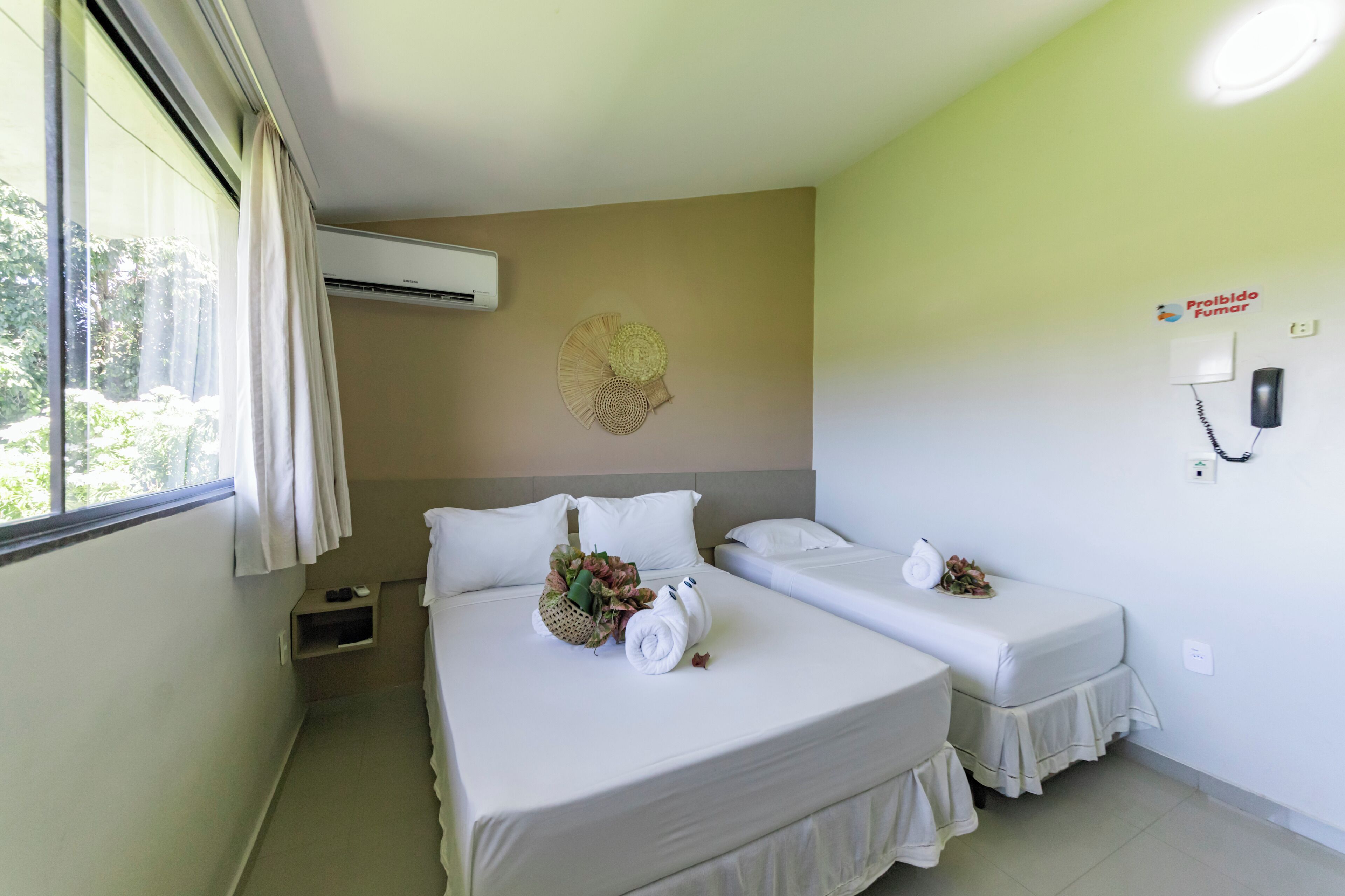 A hotel room with two beds, a window with curtains, an air conditioning unit, a wall-mounted phone, and a decorative wall piece.