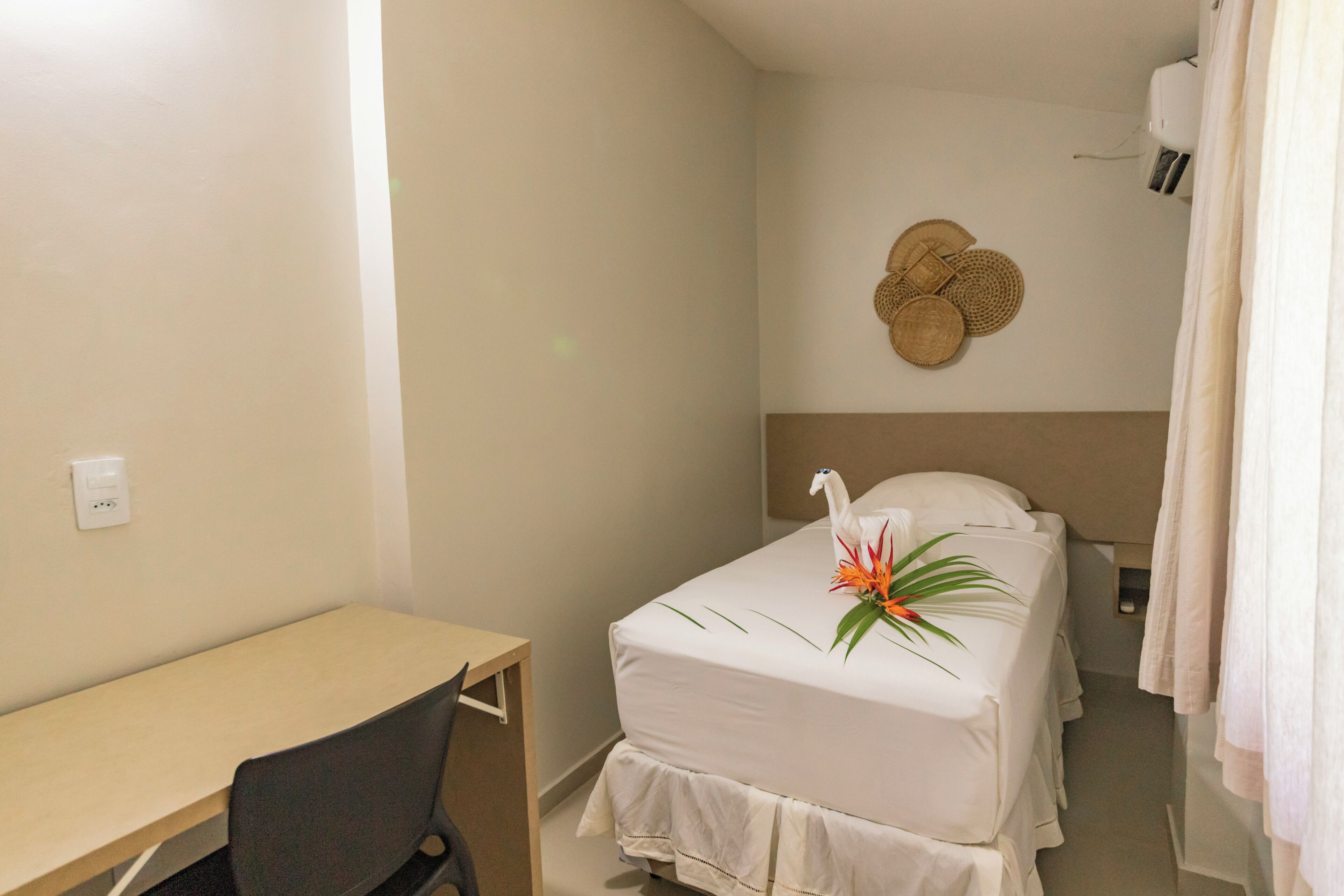A small, neatly arranged room with a single bed, a desk, and a wall-mounted air conditioning unit.