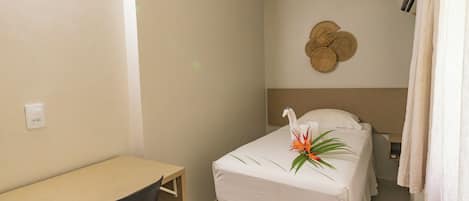 A small, neatly arranged room with a single bed, a desk, and a wall-mounted air conditioning unit.