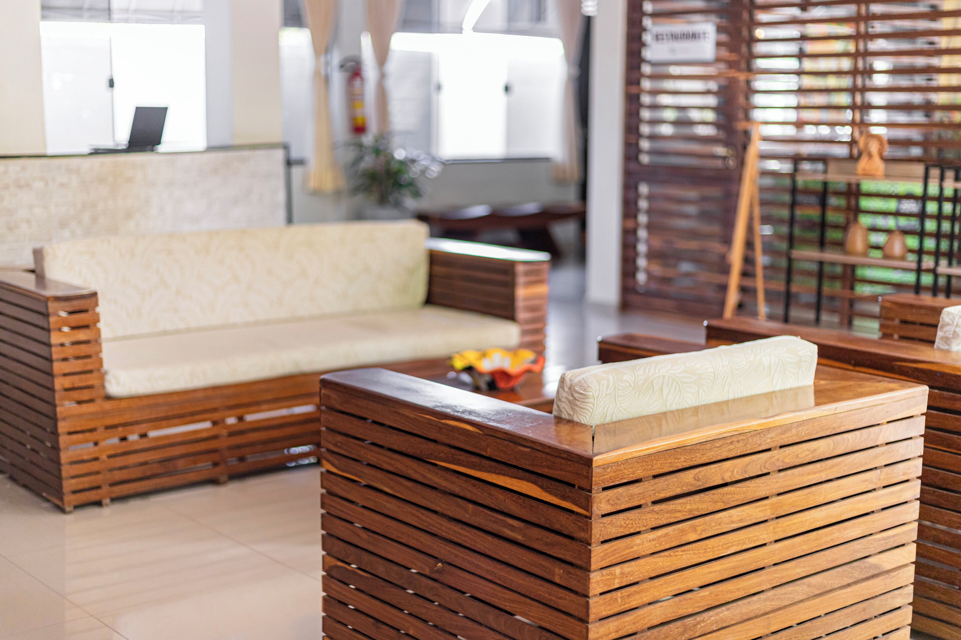 Een moderne lobby met een houten bank en bijpassende fauteuils, een receptiebalie en een decoratieve plant.