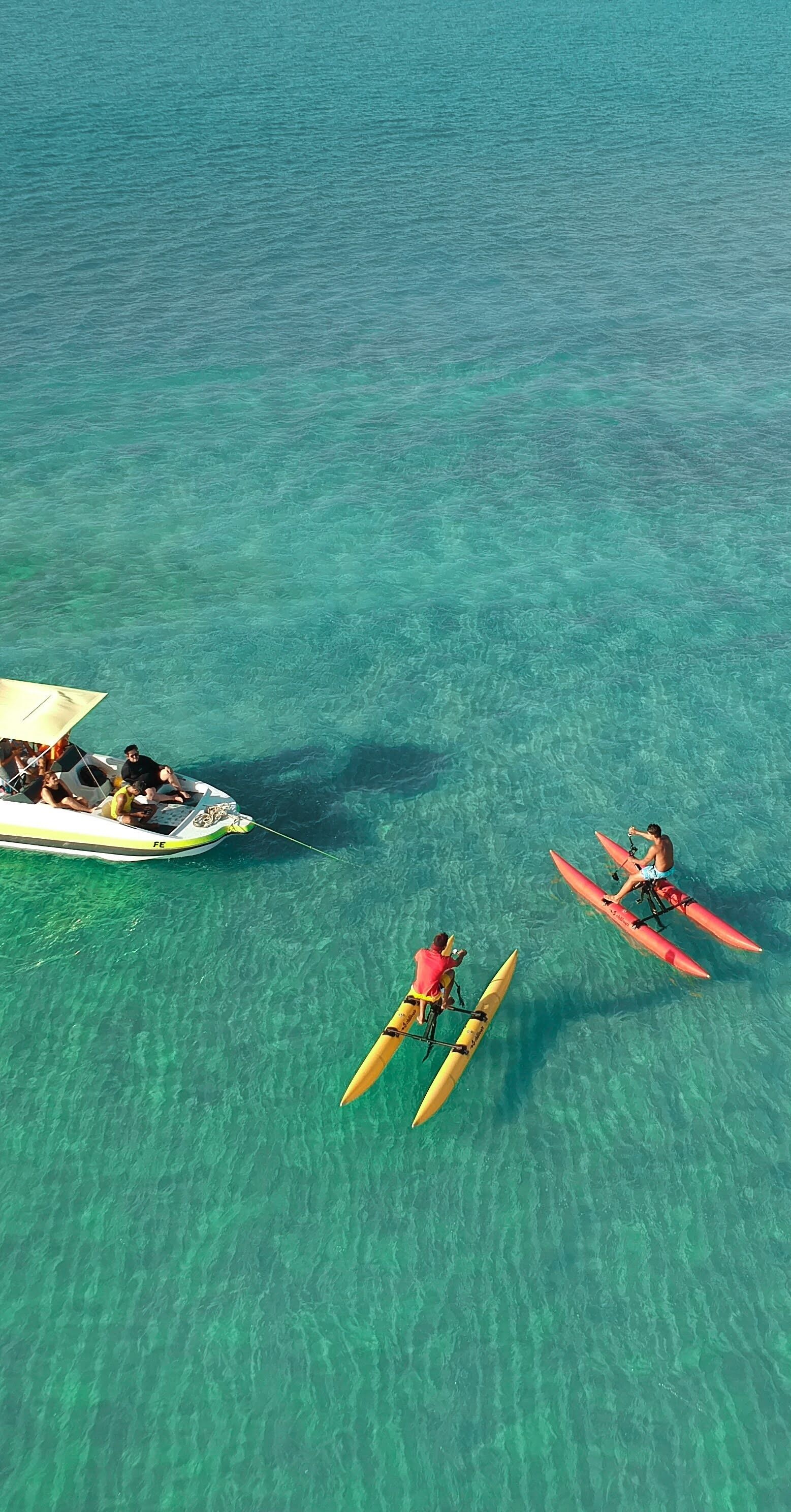 A clear turquoise sea with a boat carrying passengers and two individuals paddling on surfboards.