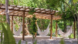 A wooden pergola with white hammocks hanging from it, surrounded by lush greenery. - Pousada Ponta de Mangue (Maragogi)