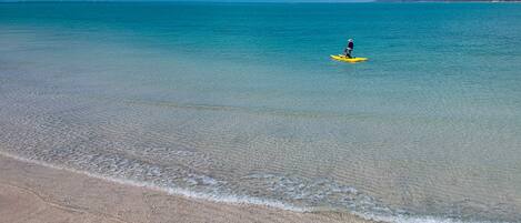 Una playa con aguas turquesas cristalinas y una persona remando en un kayak amarillo.