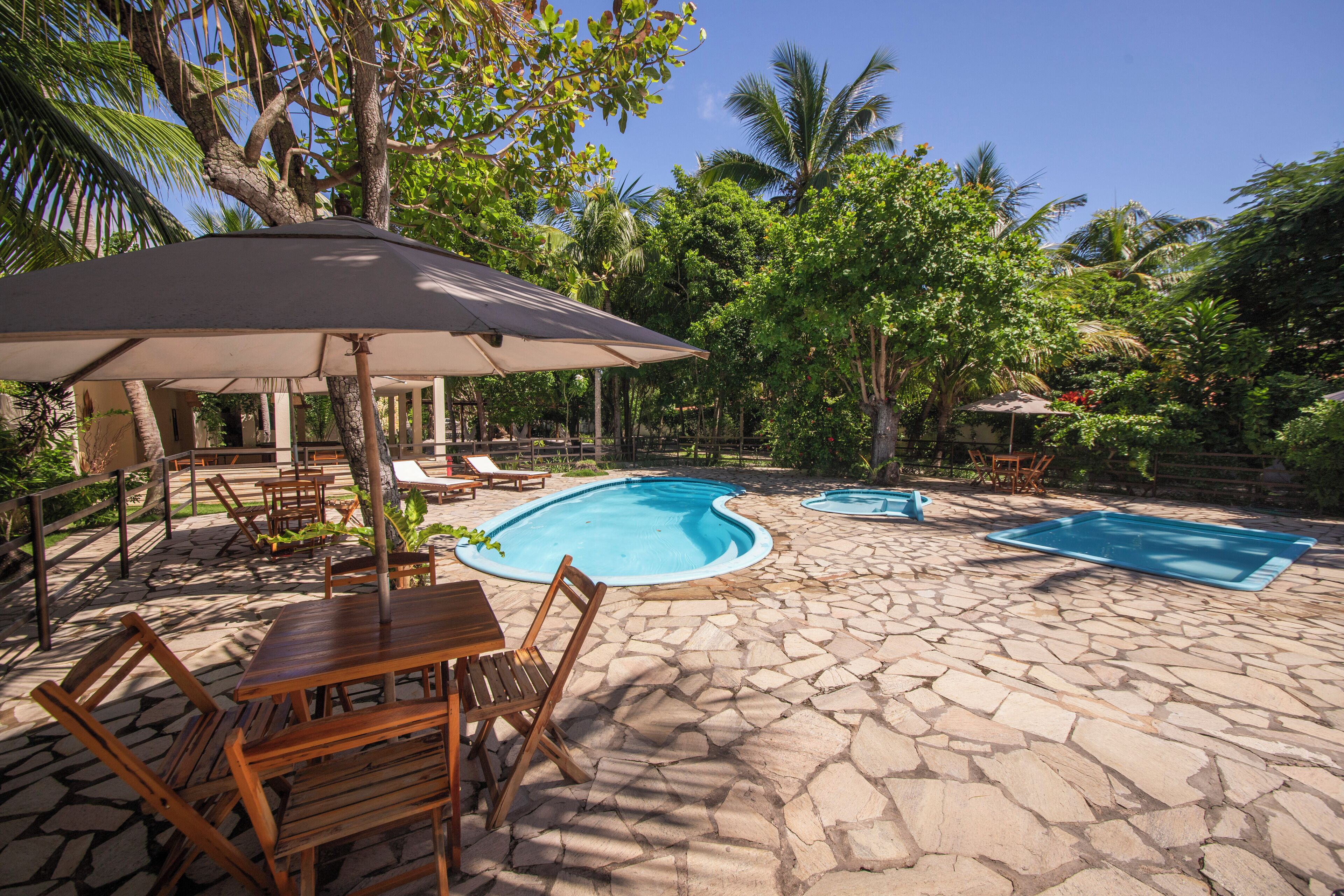 A pool area with stone flooring, wooden furniture, and an umbrella.