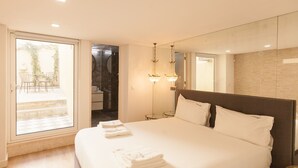 A hotel room with a large bed, a bathroom with a mirror, and a sliding door leading to an outdoor area with chairs and a table.