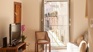 A living room with a TV, a chair, a sofa, and a balcony with a view of buildings.