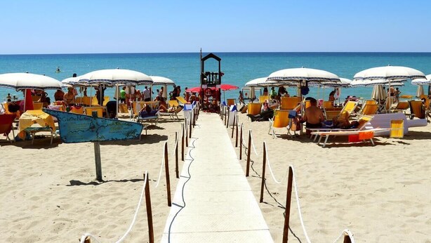 Una spiaggia con file di ombrelloni e lettini, cielo sereno e l'oceano sullo sfondo.