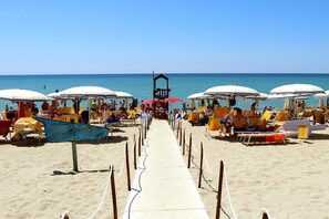 A beach with rows of sun umbrellas and lounge chairs, a clear sky, and the ocean in the background. - Nirvana Club Village (Belcastro)
