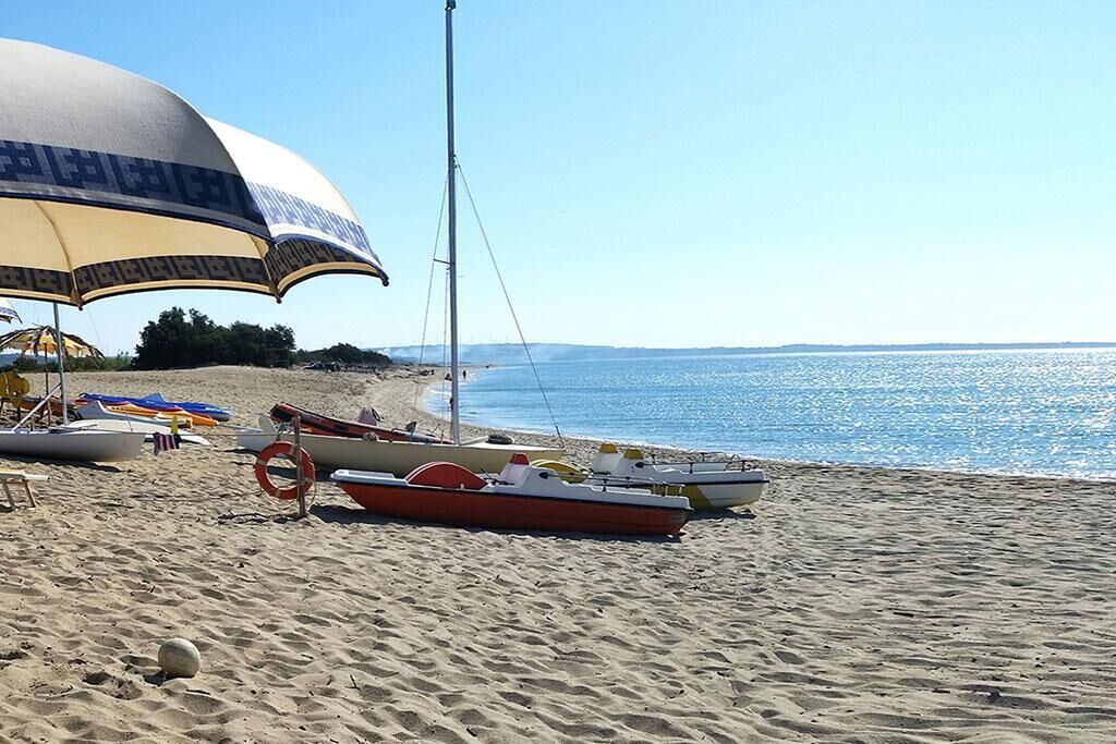 A beach with a sailboat, a lifebuoy, and a beach umbrella.