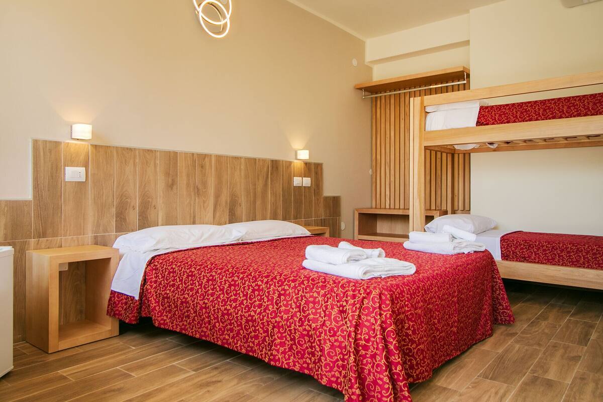 A hotel room with two beds, wooden headboards, and a red patterned bedspread.