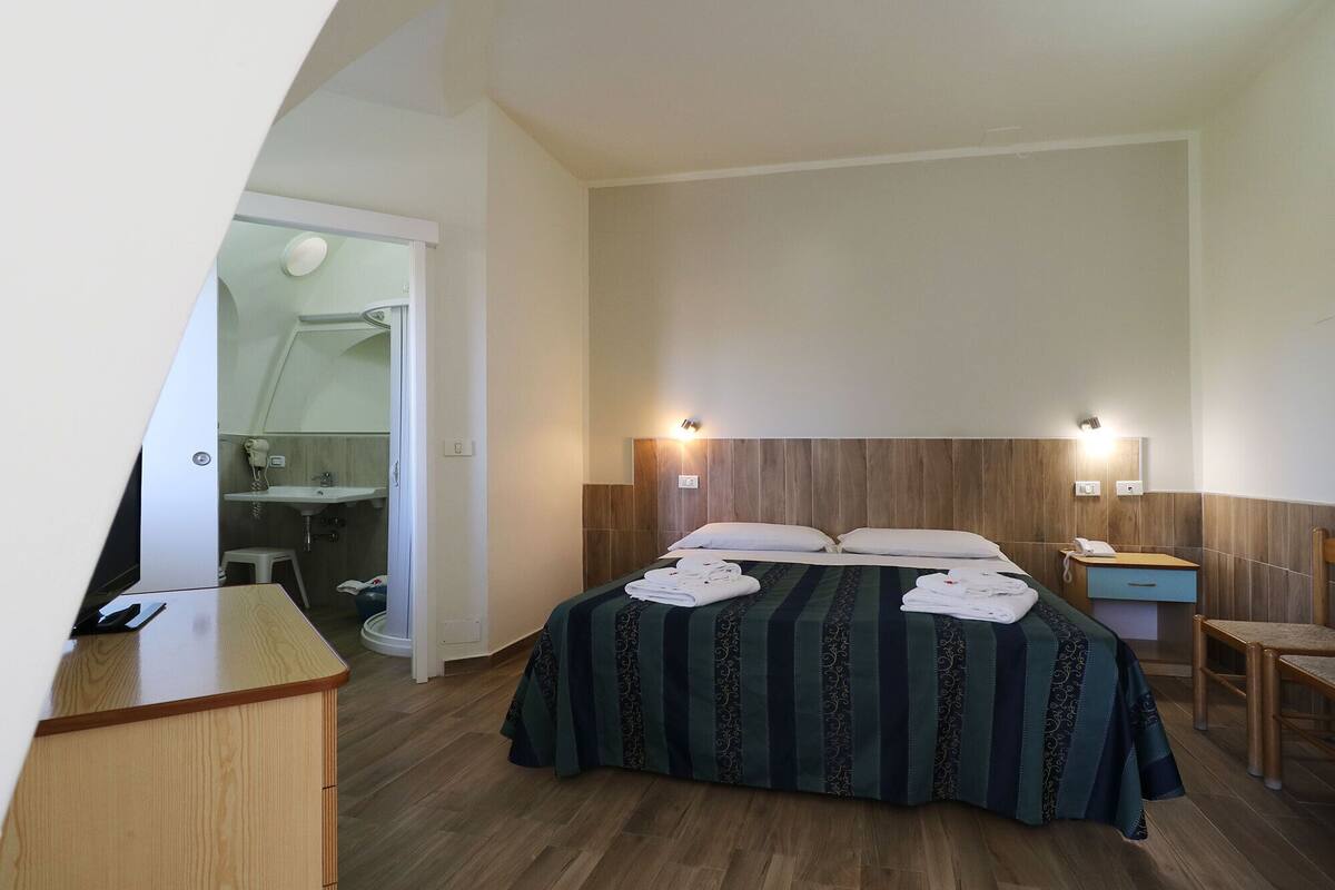 A hotel room with a bed, a desk, a chair, a bathroom, and a mirror.
