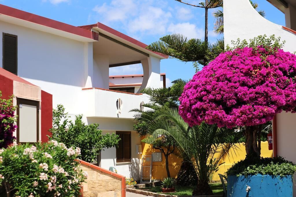 Un edificio de dos pisos con balcón, rodeado de exuberante follaje y coloridas flores de buganvilla rosa.