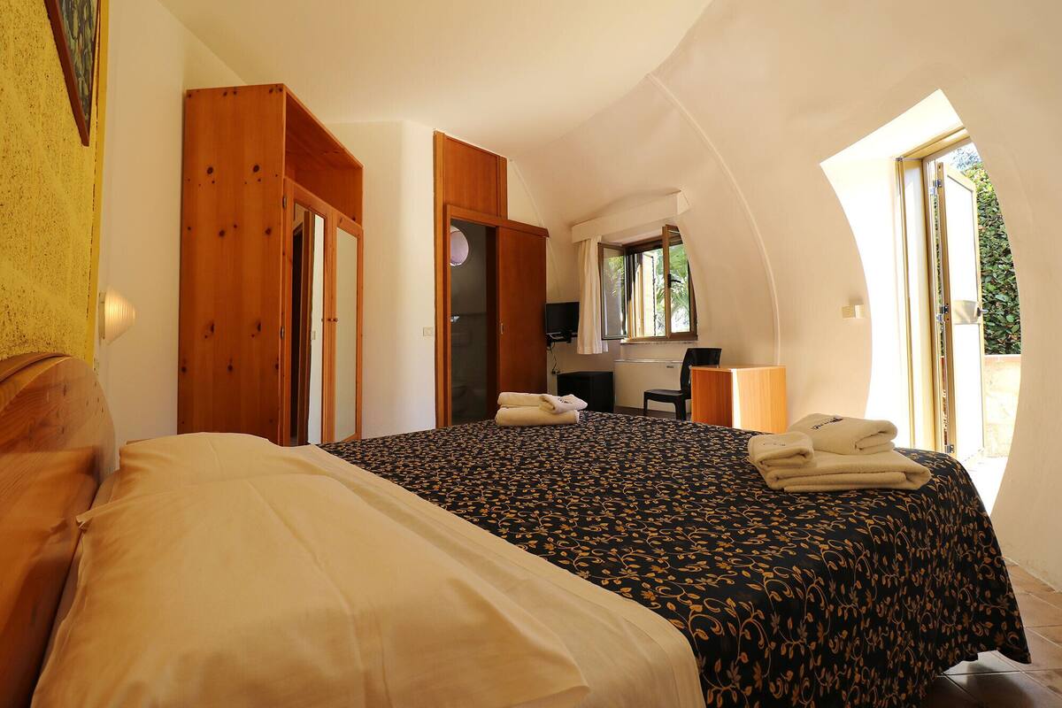 A bedroom with a bed, a desk, and a chair. There is a window providing natural light.