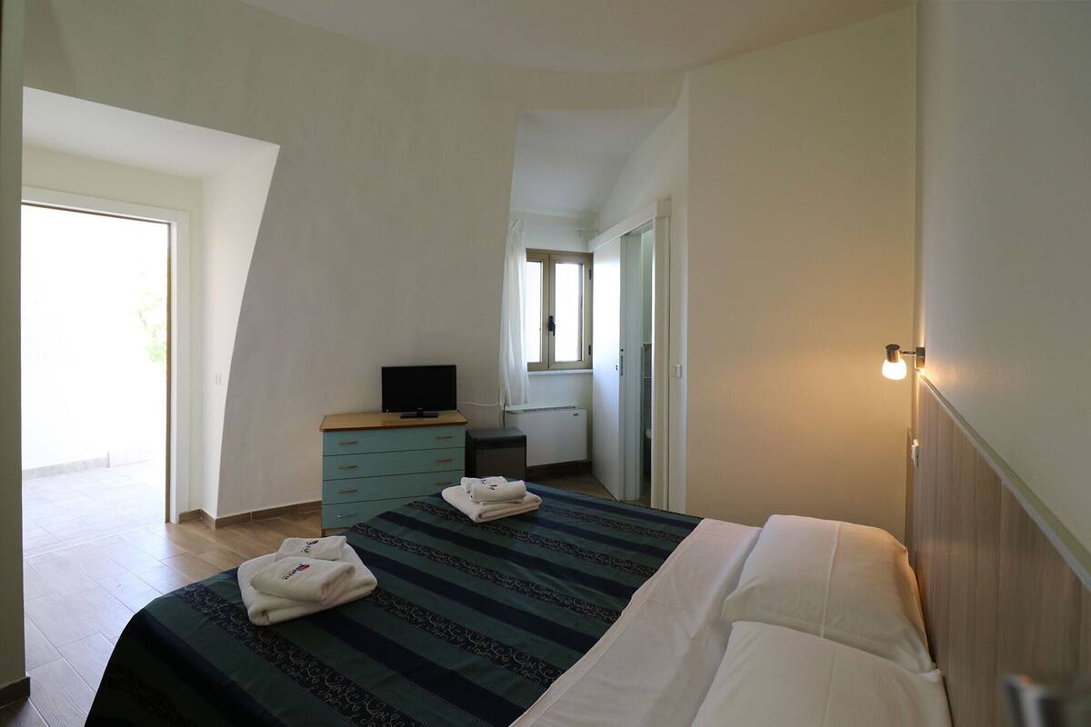 A bedroom with a bed, a dresser, a television, and a window.