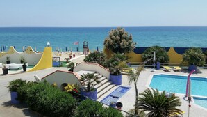 Area piscina di un resort con vista sul mare, circondata da lettini e piante in vaso.