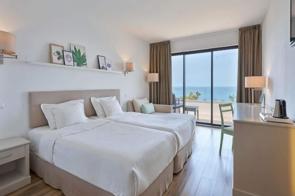 Ein Hotelzimmer mit zwei Betten, einem Schreibtisch, einem Stuhl und Meerblick.