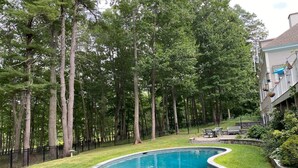 A swimming pool with a curved edge, surrounded by a well-maintained lawn and a black metal fence. - Spacious Kennebunkport River property, family/pet friendly, 2 miles to beaches (Kennebunk)